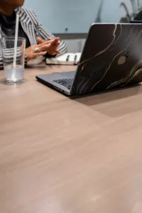Black woman web designer sitting at a table with a cup of water and a macbook discussing web design.