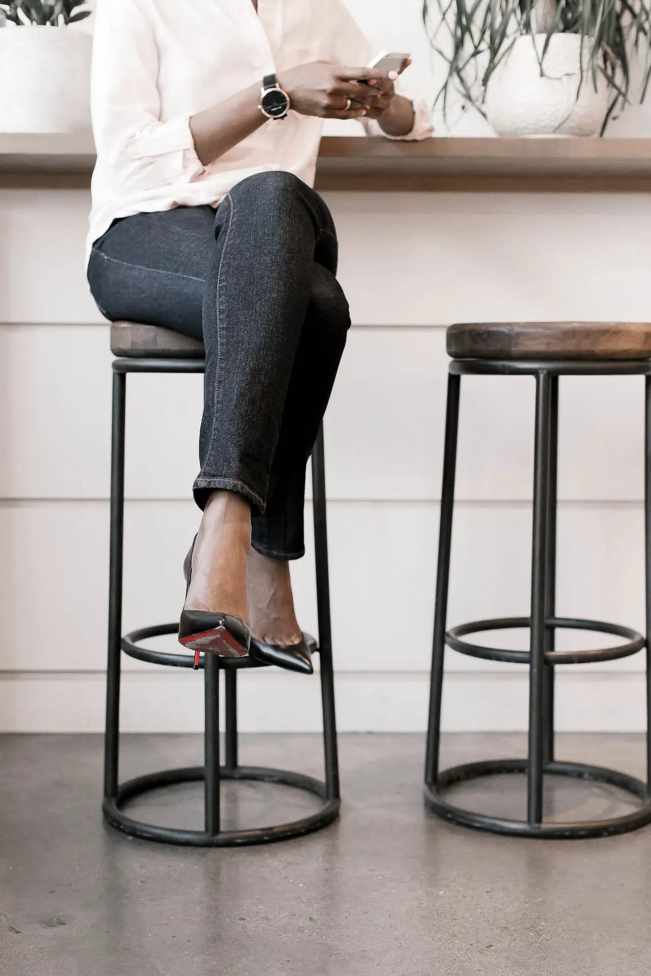 Woman sitting on bar stool with legs crossed with her cell phone in hands