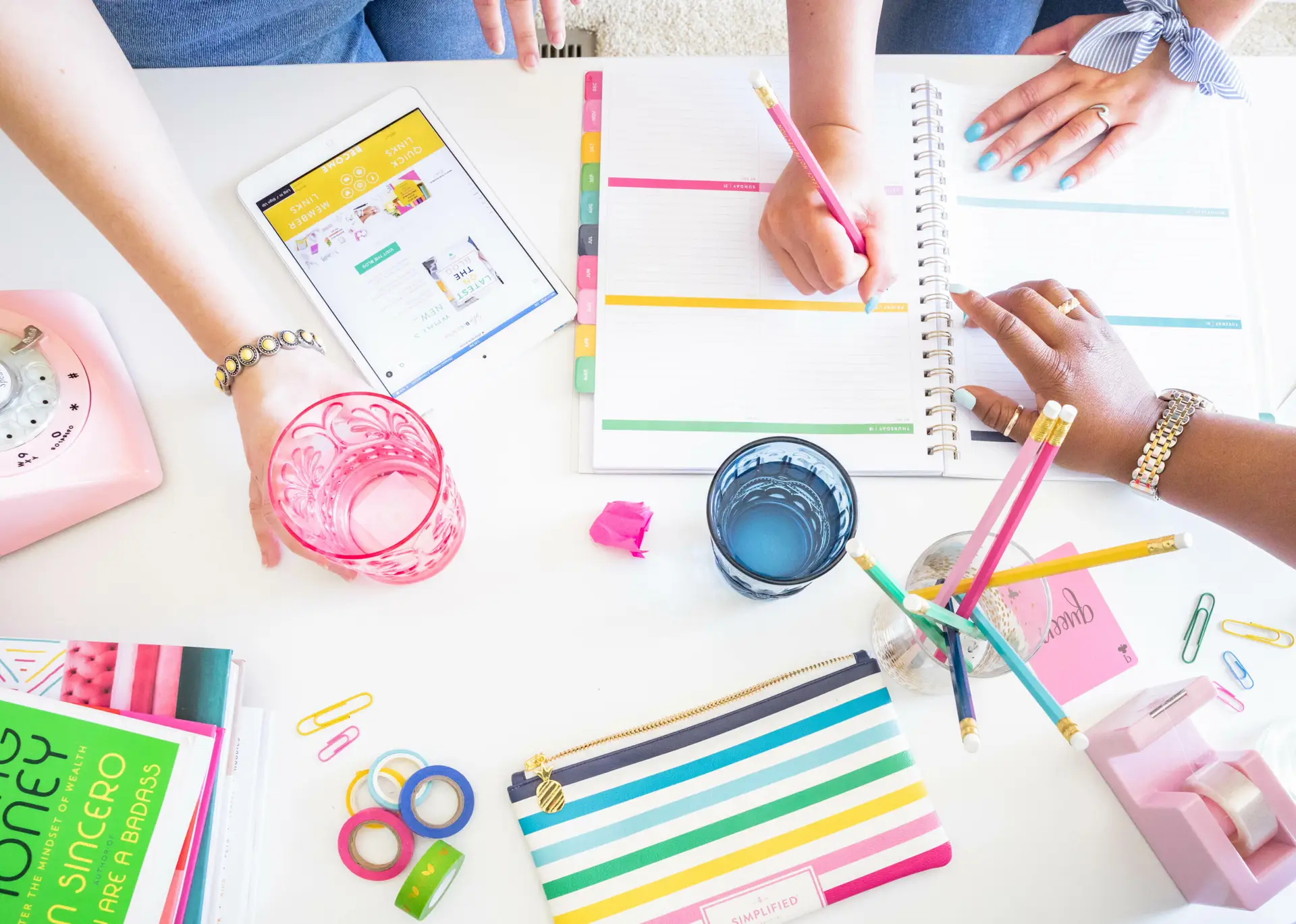 Women writing in planner and holding a cup discussing business plans.