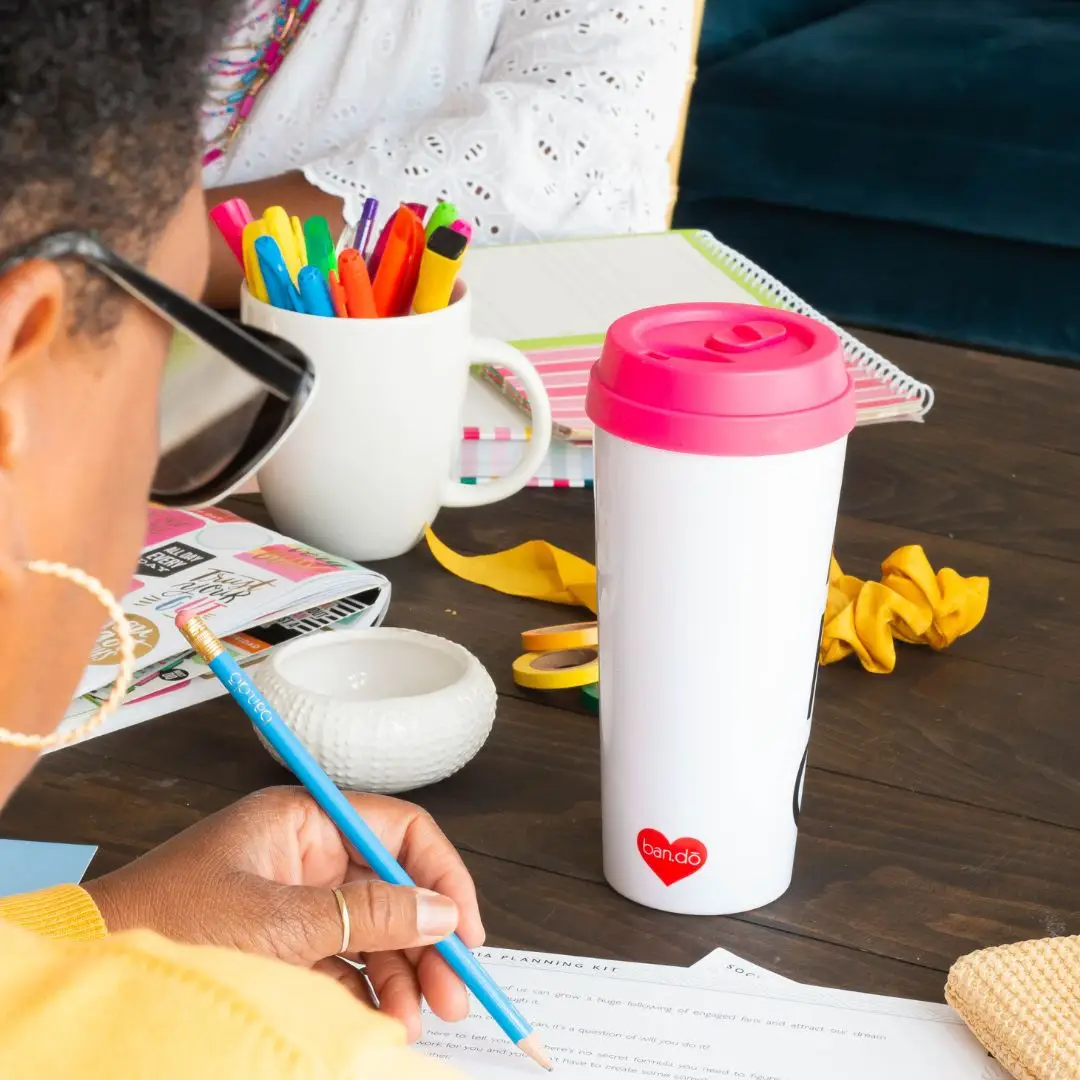 Woman sitting at a table writing with a blue pencil.