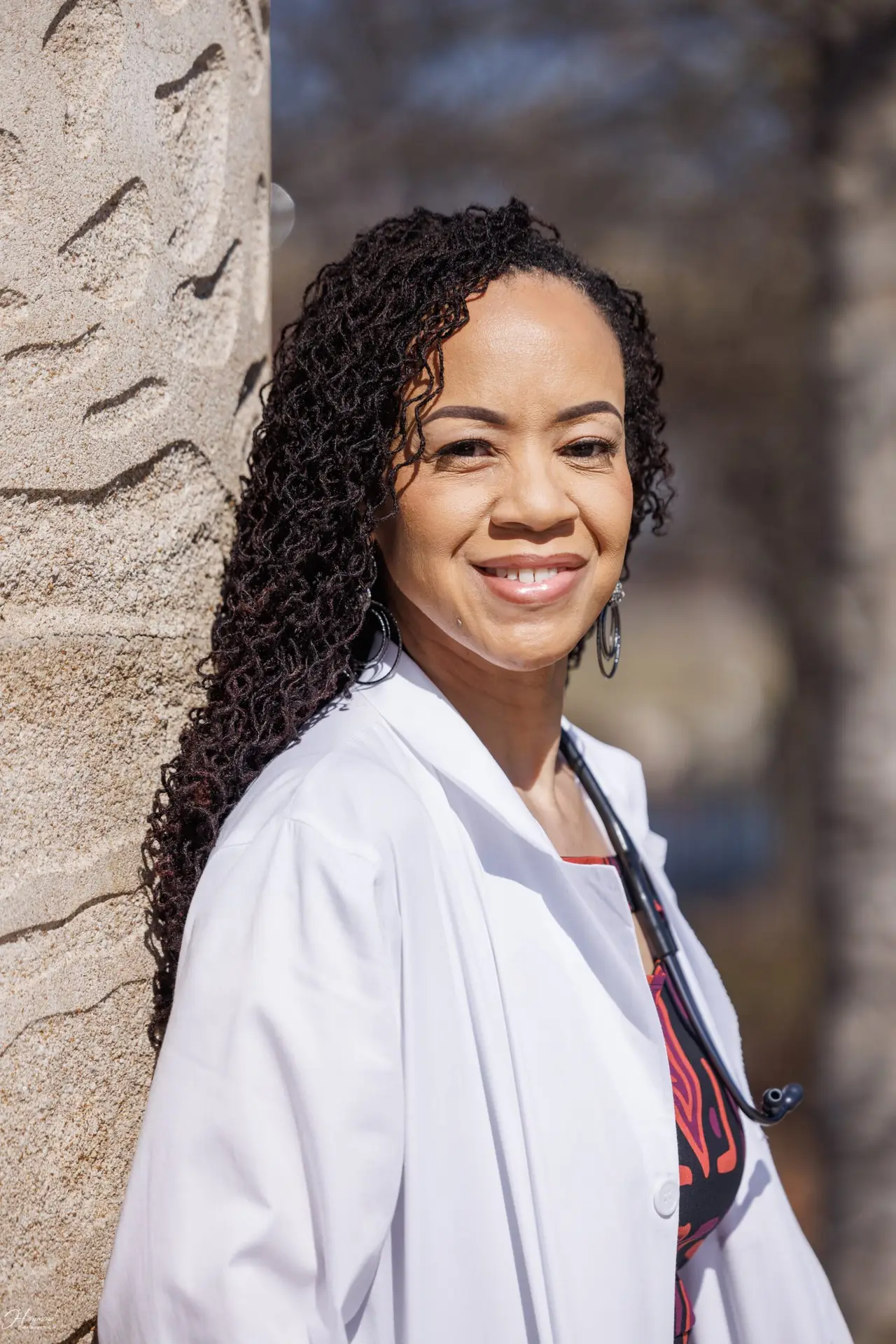 black woman in white lab coat leaning against a tree