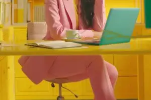 Woman in pink business pants suit sitting at a desk.